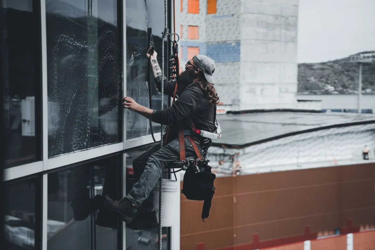 Profissional suspenso por corda limpando janelas de edifício alto
