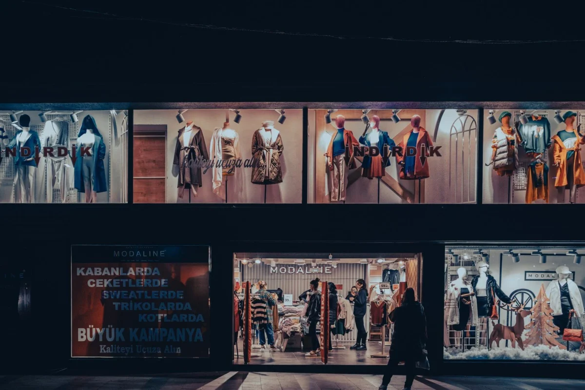 Vitrine de loja de roupas iluminada à noite, com manequins atrás do vidro